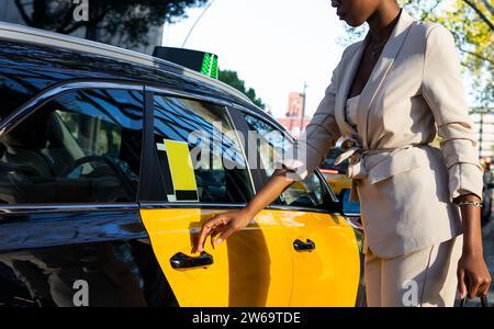 Crop anonymous African American young elegant female entrepreneur wearing formals opening taxi door while commuting to work in city Stock Photo