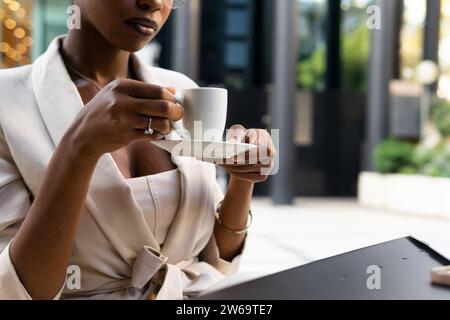 Anonymous crop African American female professional with eyeglasses holding coffee cup while sitting at sidewalk cafe Stock Photo
