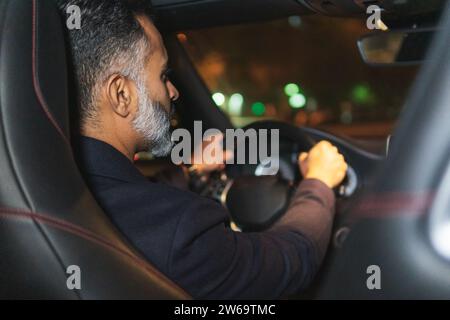 Side view of focused bearded businessman in formal clothes looking forward while driving car along street Stock Photo