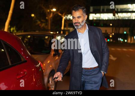 Bearded ethnic man walking towards automobile while opening with remote keyless system on city street at night Stock Photo