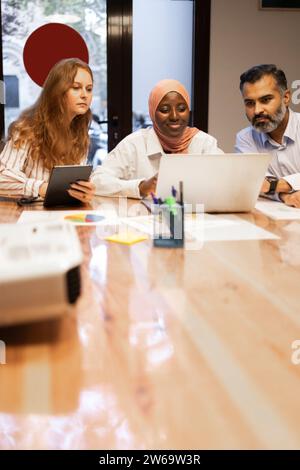 Positive young diverse colleagues while sitting at table with laptops working on a remote project in modern office Stock Photo