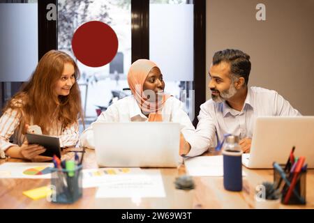 Positive young diverse colleagues while sitting at table with laptops working on a remote project in modern office Stock Photo