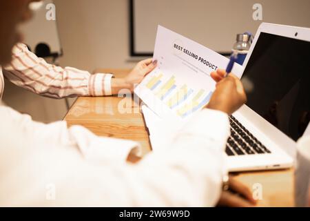 Crop faceless colleagues analyzing data on charts near laptop on desk while working in modern office during business discussion of project Stock Photo