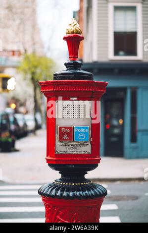 An ornate red emergency post with fire and police buttons prominently positioned on a Manhattan, New York street with city buildings in the background Stock Photo