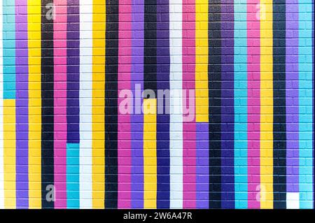 Colorful brick wall painted in various shades of pink, blue, purple, yellow, and black. Stock Photo
