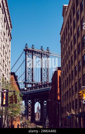 A vibrant street scene in DUMBO, Brooklyn, capturing the iconic Manhattan Bridge framed between two historic brick buildings. Stock Photo