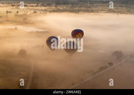 From above several colorful hot air balloons rise above a fog-engulfed landscape with the sun casting a soft glow on the scene Stock Photo