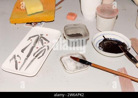From above of plastic containers with sponges and brushes with paint for pottery placed on white table Stock Photo