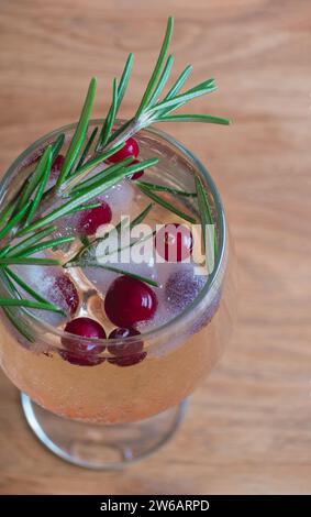 A rosemary-infused winter cocktail garnished with fresh cranberries and sprigs, served in a tall glass on a wooden surface. Stock Photo