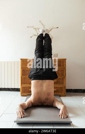 Full body of anonymous person lying on mat with raised legs and stretching hands behind back while practicing rehabilitation exercise Stock Photo