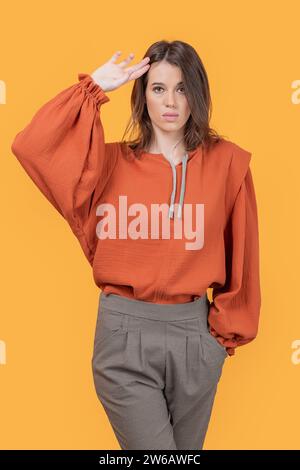 Attractive trendy young slim Caucasian woman with hand in hair looking at camera isolated on yellow background Stock Photo