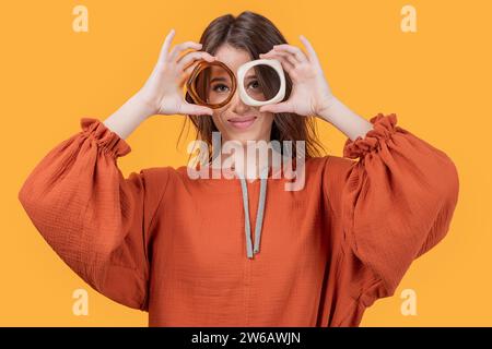 Smiling Caucasian young woman in casual making eyeglasses with bangles looking at camera isolated on yellow background Stock Photo
