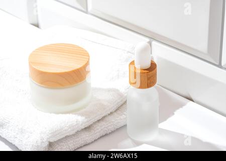 A serene setting showcasing two skincare products with wooden caps, stylishly positioned on a white towel beside a window with light pouring in Stock Photo