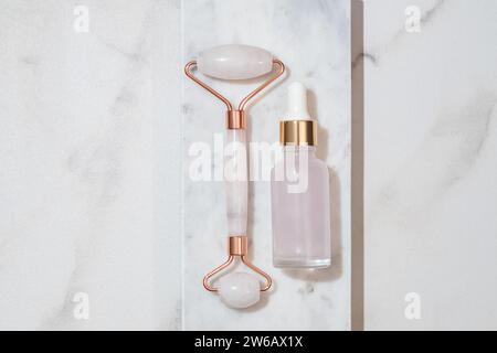 Elegant rose quartz facial roller paired with a serum bottle, set against a luxurious marble backdrop Stock Photo