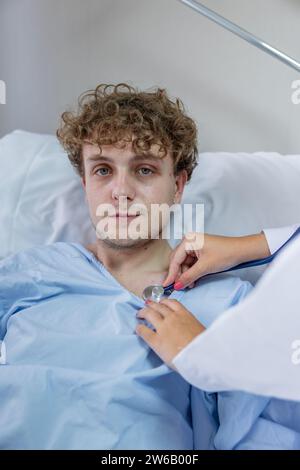 Crop doctor checking heartbeat with stethoscope on patient lying on bed and looking at camera in hospital during check up Stock Photo