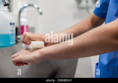 Crop faceless nurse in uniform washing hands with sponge on blurred background of sink at hospital Stock Photo