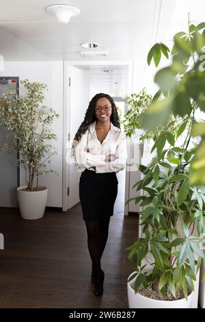 Full body portrait of happy young African American businesswoman standing confidently with arms crossed in office Stock Photo