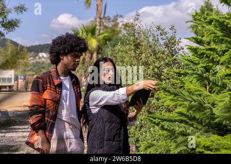 Confident young farmers in jackets discussing over digital tablet while working in organic greenhouse Stock Photo