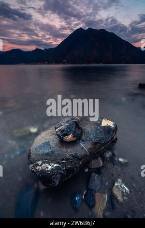 Close-up of rocks along lakeshore of Lake Como with mountain backdrop, Argengo, Lombardy, Italy Stock Photo