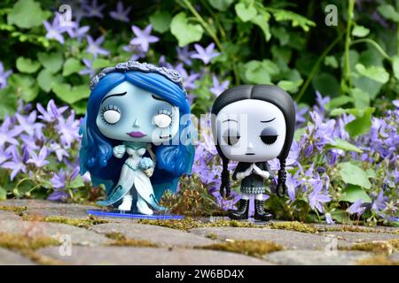 Funko Pop action figures of Emily from dark fantasy gothic animated film Corpse Bride and Wednesday Addams. Blue flowers, green moss, mysterious. Stock Photo