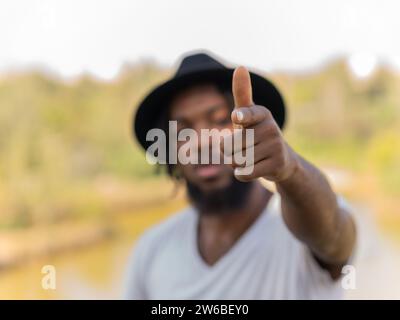 Soft focus of bearded African American guy in hat and white t shirt pointing finger at camera while standing outdoors Stock Photo