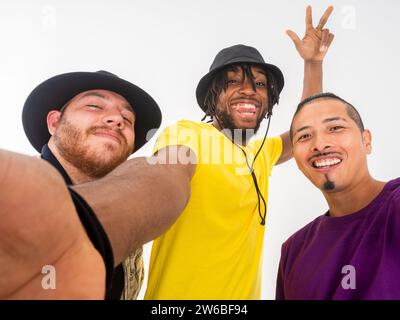 Three cheerful young men pose for a playful selfie, smiling and showing peace signs to the camera on a white background Stock Photo