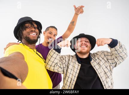 Three cheerful young men pose for a playful selfie, smiling and showing peace signs to the camera on a white background Stock Photo