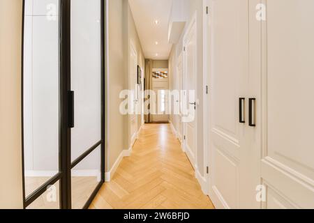 Interior of empty long hallway with white closed doors of rooms and parquet floor at contemporary light house Stock Photo