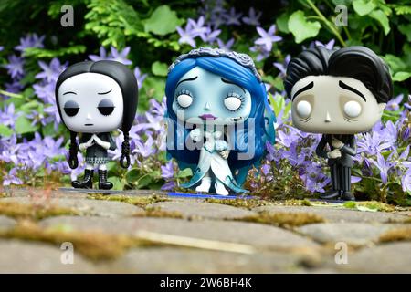 Funko Pop action figures of Victor and Emily from dark fantasy gothic animated film Corpse Bride and Wednesday Addams. Blue flowers, green moss. Stock Photo