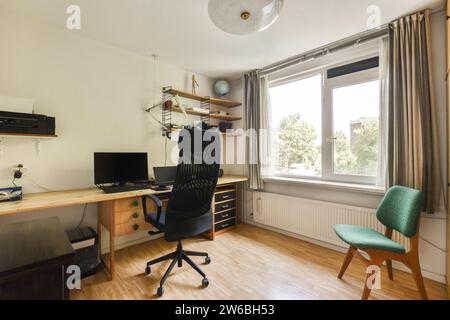 Computer and laptop on wooden desk in modern den of luxurious apartment with chair and window Stock Photo