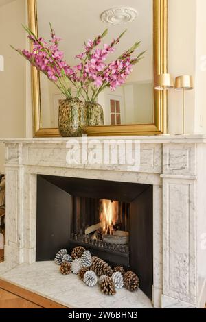 Flower vase and mirror on mantel with fire burning in fireplace inside living room at modern apartment Stock Photo