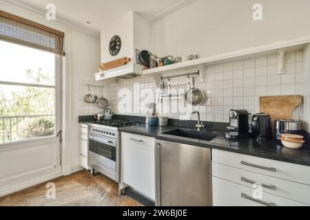 Stainless steel utensils and appliances on countertop in modern kitchen with white shelf and wall Stock Photo
