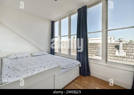 Blue curtains on windows besides large bed with pillows in white bedroom of modern apartment Stock Photo