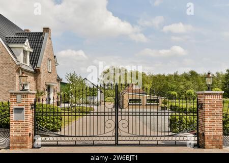 Closed wrought iron gate with empty driveway of contemporary bungalow against sky on sunny day Stock Photo