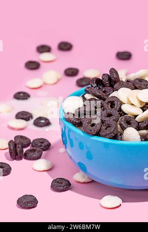 A vibrant bowl filled with chocolate cookies and white baking chips against a pink background, with some scattered around. Stock Photo
