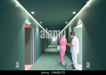 Female nurse in pink uniform and mask and male surgeon discussing over reports while standing at empty passage in modern hospital Stock Photo