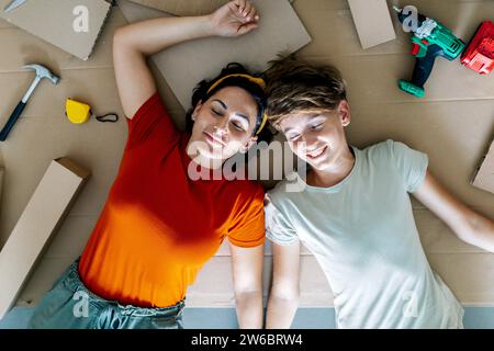 Top view of delighted woman and son lying on floor eyes closed and smiling during relocation into new flat Stock Photo