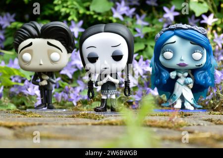 Funko Pop action figures of Victor and Emily from dark fantasy gothic animated film Corpse Bride and Wednesday Addams. Blue flowers, moss, stone road. Stock Photo