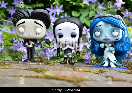 Funko Pop action figures of Victor and Emily from dark fantasy gothic animated film Corpse Bride and Wednesday Addams. Blue flowers, moss, stone road. Stock Photo