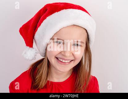 Little Girl In Red T-Shirt And Santa Hat Poses For A Festive Photo On A White Background Stock Photo