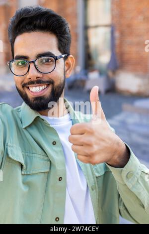 Vertical close-up photo of a smiling young Indian man talking on the phone on a video call, recording a blog, smiling at the camera and showing super. Stock Photo