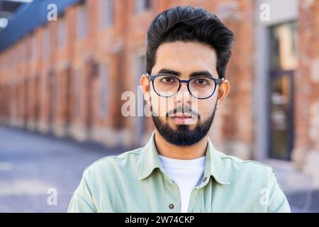 A close-up portrait of a young Indian man standing outside on his forehead and looking seriously into the camera. Stock Photo
