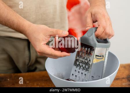 Person grating fresh beet, hands covered in juice, meal preparation. Stock Photo