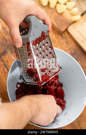 Preparing ingredients: vibrant beet staining hands while grating. Stock Photo