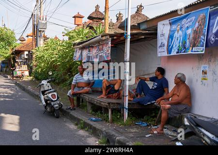 People resting near the road in an unusual Asian village. Children are playing and adults are talking sitting on the roadside. Bali, Indonesia - 11.30 Stock Photo