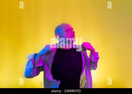 Bearded, bald man opening his shirt. Isolated on yellow background. Stock Photo