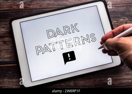 Keyword “Dark Patterns” seen on tablet on wooden table. Man hand holding wireless stylus pen. Deceptive online business practice concept Stock Photo