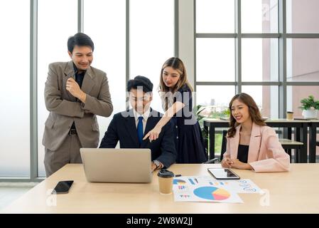Business professionals collaborating with enthusiasm while examining data on a laptop in a contemporary office setting. Stock Photo