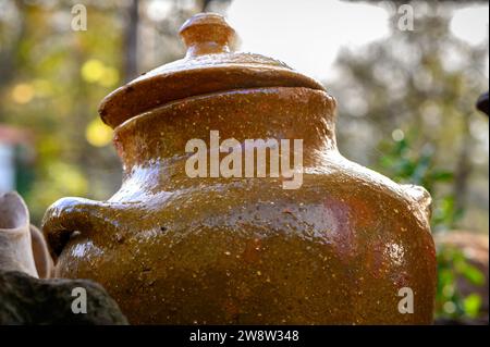 Close-up of a reddish fired clay cooking pot or pot with its small lid, in the light of the evening, with the greenery of the garden and trees Stock Photo