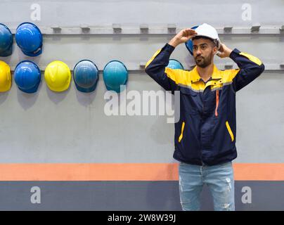 Young man working in a factory,  wearing construction hardhat on his head for safety. Concept of work safety. Building industry. Stock Photo